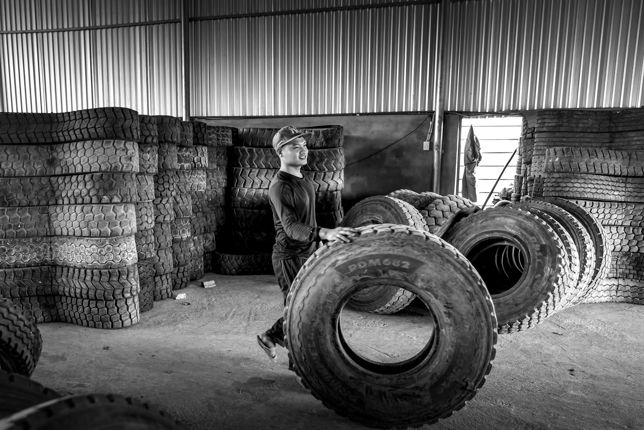 Man in black and white monochrome scene with stacked tires in industrial setting.