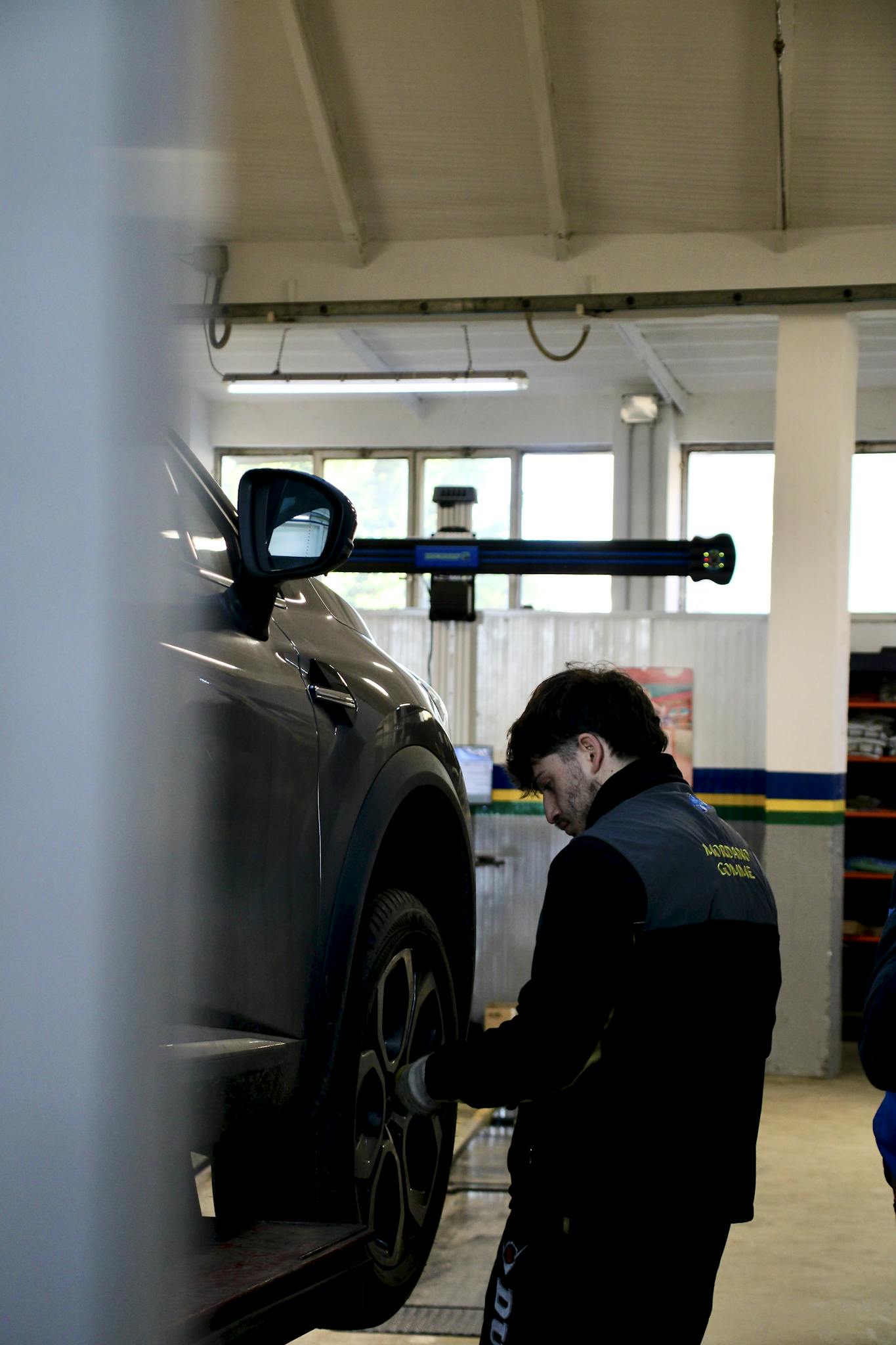 Mechanic adjusting car tire on lift in an indoor workshop setting.
